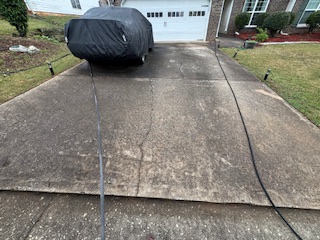 Dirty concrete driveway covered in dark algae and tire marks before pressure washing in Ellenwood, GA