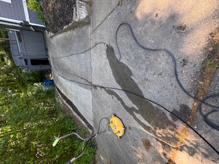 Stained concrete driveway with hoses and a covered vehicle parked near the garage before cleaning.