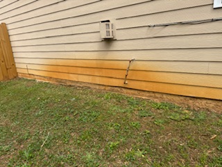 Dark, weathered pavers with grass in the joints beside a brick wall before cleaning.