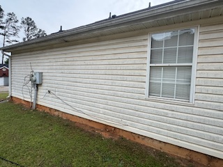 Tan lap siding with mildew and mud staining along the bottom edge before house washing.