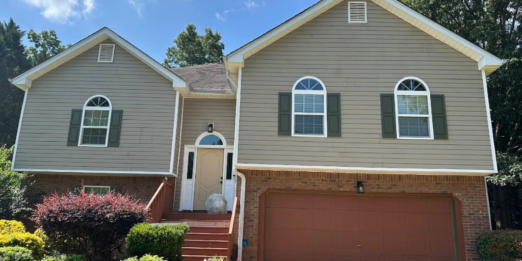 Front of a split-level home with tan siding, brick, garage, and landscaping.
