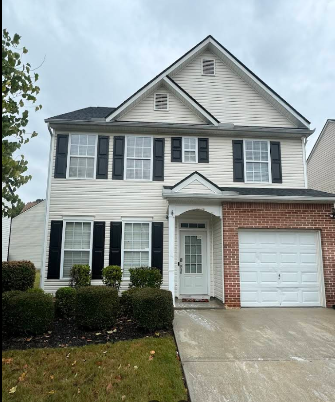 Front of a two-story home with light siding, brick around the garage, and landscaping.