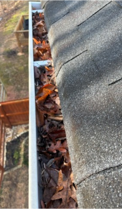 Roof gutter packed with dry brown leaves blocking drainage along the eave